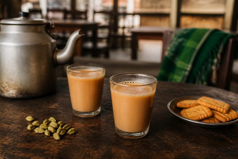Zwei Gläser pakistanischer Milchtee mit Metallkanne, Kardamom und Gebäck